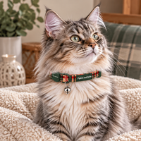 A fluffy long-haired cat wearing a green and red plaid collar with a small bell, sitting on a cream sherpa blanket in a cozy indoor setting.