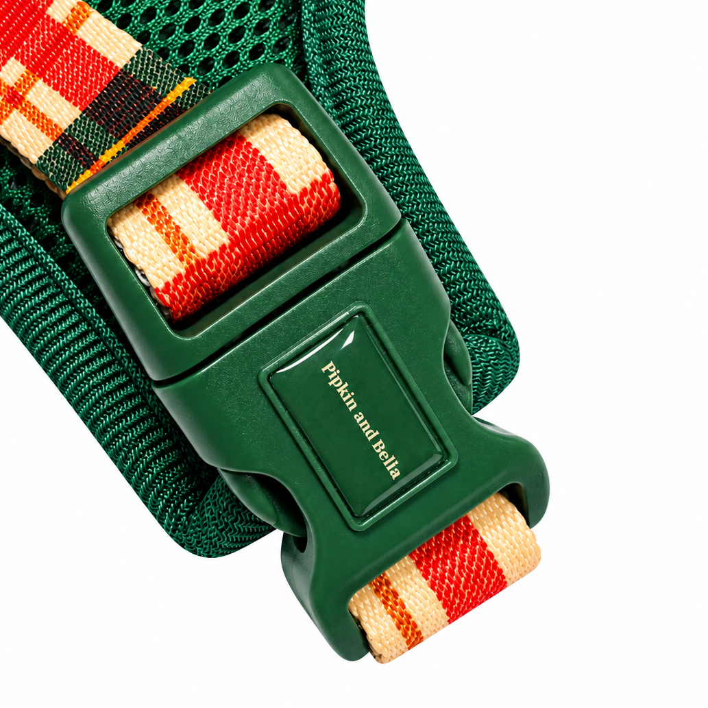 Close-up of a green mesh pet harness with a red, beige, and green plaid webbing strap and a green plastic buckle. The buckle has the brand name 'Pipkin and Bella' embossed on it.